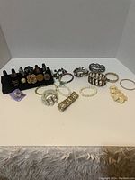 Full view of 11 assorted costume rings and bracelets arranged on a white surface with a black ring display stand holding most rings.