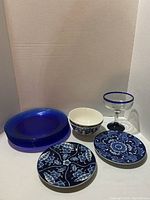 The full set showing 6 blue glass dinner plates stacked, 2 Royal Norfolk blue floral bowls, 2 Giftcraft decorative plates with blue floral design, and a blue rimmed margarita glass.