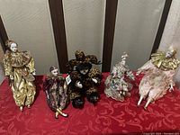 Five porcelain clown and jester dolls arranged on red fabric, showing varied costumes and one cheetah-themed doll in the middle.