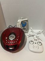 Red Emerson PD6870RD portable CD system, iGym pedometer in packaging, white drone with controller on white background