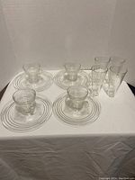Photo showing 4 plates, 4 cups, and 4 drinking glasses with ribbed circular design.