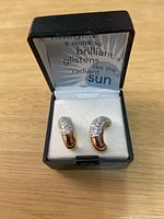 Pair of curved 14 KT gold plated earrings with white CZ stones displayed in a black jewelry box with padding.