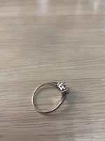 Ring displayed on wooden surface showing prong setting for missing center stone and accent stone.