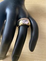 Ring displayed on a black mannequin hand showing the gold-plated band and pink stone on the middle finger.
