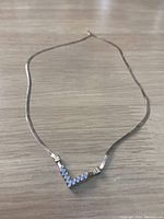 Photo showing the full 16-inch gold chain necklace laid flat with a V-shaped pendant featuring clear stones.