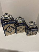 Front angle of three ceramic cobalt blue embossed canisters of varied sizes arranged in a line showing detailed design and condition