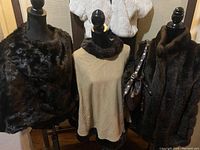 Three mannequins displaying a brown faux wrap cape, beige sleeveless vest with dark collar trim, and a brown faux sleeveless coat with a Metro 7 handbag over the shoulder.