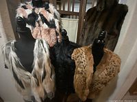 Five pieces of ladies warm faux fur clothing including four vests and one jacket. Vests shown on mannequins with distinct colors and patterns. The larger jacket shows a striped brown fur pattern and collar.