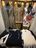 Seven assorted ladies sweaters displayed on three mannequins and laid out, showing various styles and patterns including stripes, leopard print, floral tattoo design, and ruffles.