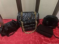 Five assorted black handbags laid side by side showing size and style differences, including soft quilted patterns and chain straps.