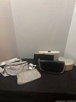 Five purses displayed with the silver heart-shaped jewelry box all on a black surface against a light grey backdrop.