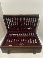 Open wooden chest with silverware arranged in maroon felt slots.