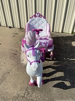 Front view of pink and white horse and carriage ride-on toy showing seated area, steering wheel, and horse with pink feather plume.