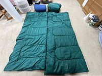 Two green sleeping bags laid open side by side with their carrying sacks nearby.