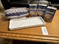 Full view of the Conair hot roller set, white rollers with clips, three Goody perm rods boxes and white tray on wood table