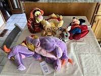Full set of five Disney character hand puppets and plush toys on a white table, showing Figment, Mickey Mouse, Dodger, Tigger, and Winnie the Pooh.