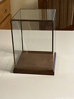 Overall view of the assembled glass display case on wooden base on white table against kitchen background.