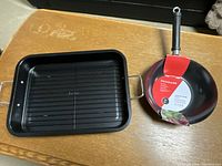 Photo showing the black rectangular Oster roasting pan alongside the Frigidaire stir fry wok in packaging.