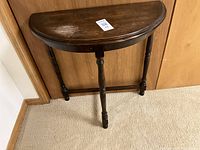 Front view of the half moon wooden side table showing turned legs and worn top surface.