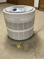 Front side view of the white cylindrical Honeywell air purifier showing vent slats and power cord with tag.