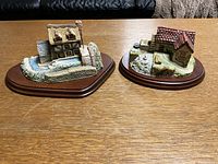 Two Memory Lane cottages, Trout Leap and Dove Mill, displayed on a wooden surface showing fronts and water feature detail on Trout Leap.