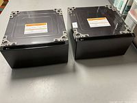 Top view of both black LG pedestals showing metallic tops with warning labels, sitting side by side on floor.