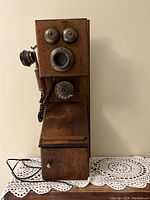 Front view of wooden replica wall-mounted telephone showing bells, mouthpiece, rotary dial, and drawer.