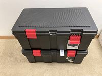 Two black storage lockers stacked, one on top of the other, both closed, showing the red latches.