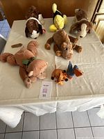 Photo showing all 7 TY animal plush toys arranged on a table, including dogs, a camel, fish, monkey, giraffe, and pelican.