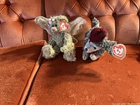 Front view of Cheri the dog and Angel the bear Ty Beanie Babies with tags on an orange couch