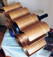 Close side view of wooden bentwood wine rack holding bottles horizontally on wavy shelves.