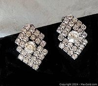 Close-up image of a pair of silver-tone Art Deco rhinestone clip earrings with a diamond design and a larger central rhinestone.