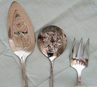 Photo showing three silver serving pieces: pierced spatula, decorated slotted spoon, and serving fork.