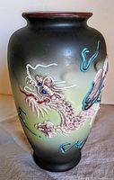 Front view of the vase showing the detailed dragon motif with blue jewel eyes on a gradient black and green background.
