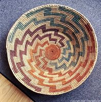 Top-down view of the basket showing detailed zigzag pattern in natural, rusty red, purple, and blue tones on woven fibers.