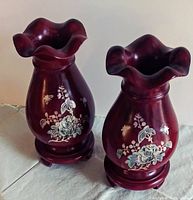 Pair of dark reddish-brown wooden vases with fluted tops and detailed floral inlay work, shown standing on a light-colored cloth surface.