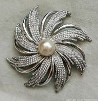 Front view of vintage silver-tone round sunburst brooch with textured and smooth rays and centrally set white imitation pearl.