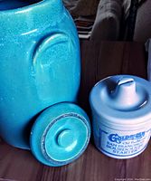 Close-up image showing large plain turquoise crock with lid and small white crock labeled 'Goldrush San Francisco Sourdough Starter' with lid