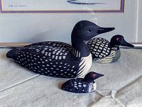 Three hand-carved wooden loon decoys in small, medium, and large sizes showing detailed paint and red eyes.