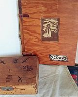 Photo showing the front top view of the two wooden storage pieces, the smaller box with hand-tooled nautical decorations and the larger wooden covered 'SCRAPS' book with sailboat image.