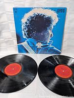 Two black vinyl records with red labels laid out in front of album cover.