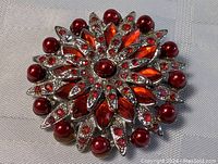 Front view of the red burst pin brooch showing arrangement of red rhinestones and beads on silver-tone metal base.