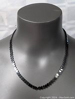 Front view of black shiny heart-shaped linked necklace displayed on a mannequin bust.
