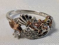 Close-up showing sterling silver 925S stamp, mermaid design with rose gold highlights, clear stones, and size 7 marking inside band.