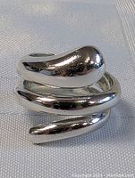 Close-up photo of a shiny sterling silver spiral ring on a light textured fabric background. The ring has a smooth polished finish and a modern swirl design.