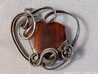 Close-up of sterling silver pendant with brown gemstone showing swirling silver details and setting condition