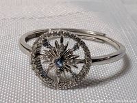 Top angled view showing round face with central blue topaz, diamond chips around the edge, and starburst design in sterling silver.