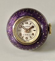 Front view of the Bucherer pendant watch showing the purple enamel case with gold tone detailing and white dial.