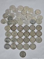 Top-down view of 49 silver-coloured Canadian 25-cent coins on white background showing mixed obverse and reverse.