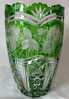 Front view of emerald green crystal vase with sawtooth cut clear crystal border and floral etching around the body.